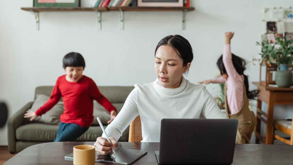 busy mom working on laptop and noisy children running around